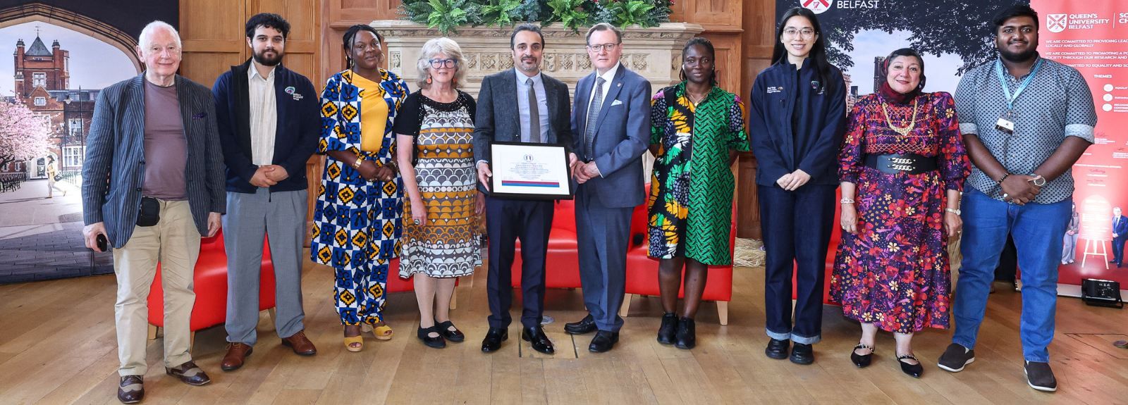 Diverse group of people standing, the one in the middle holds the framed certificate of University of Sanctuary