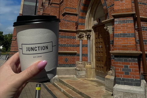 Student holding cup from Junction cafe in front of Grad School