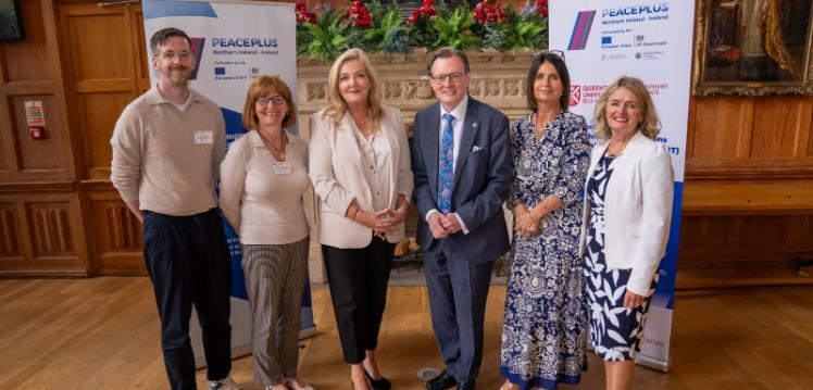 Three women and two men stand in front of a fireplace in a grand historic university room