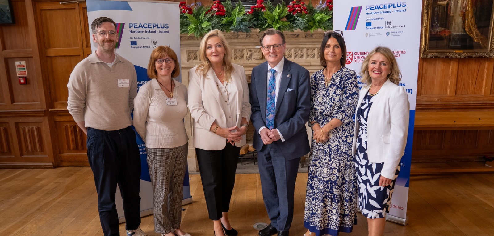 Three women and two men stand in front of a fireplace in a grand historic university room