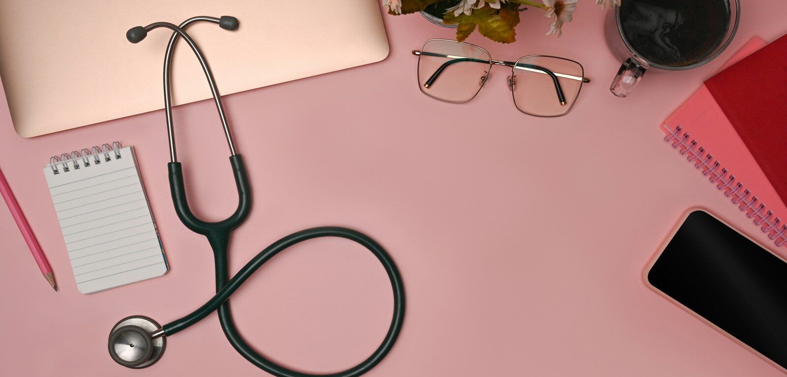 Stethoscope, pair of glasses and notebook on top of pink desk