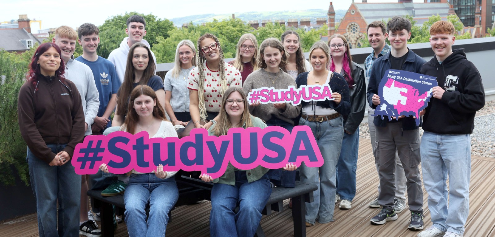 A group of students stand on a rooftop holding Study USA signage and smiling towards the camera
