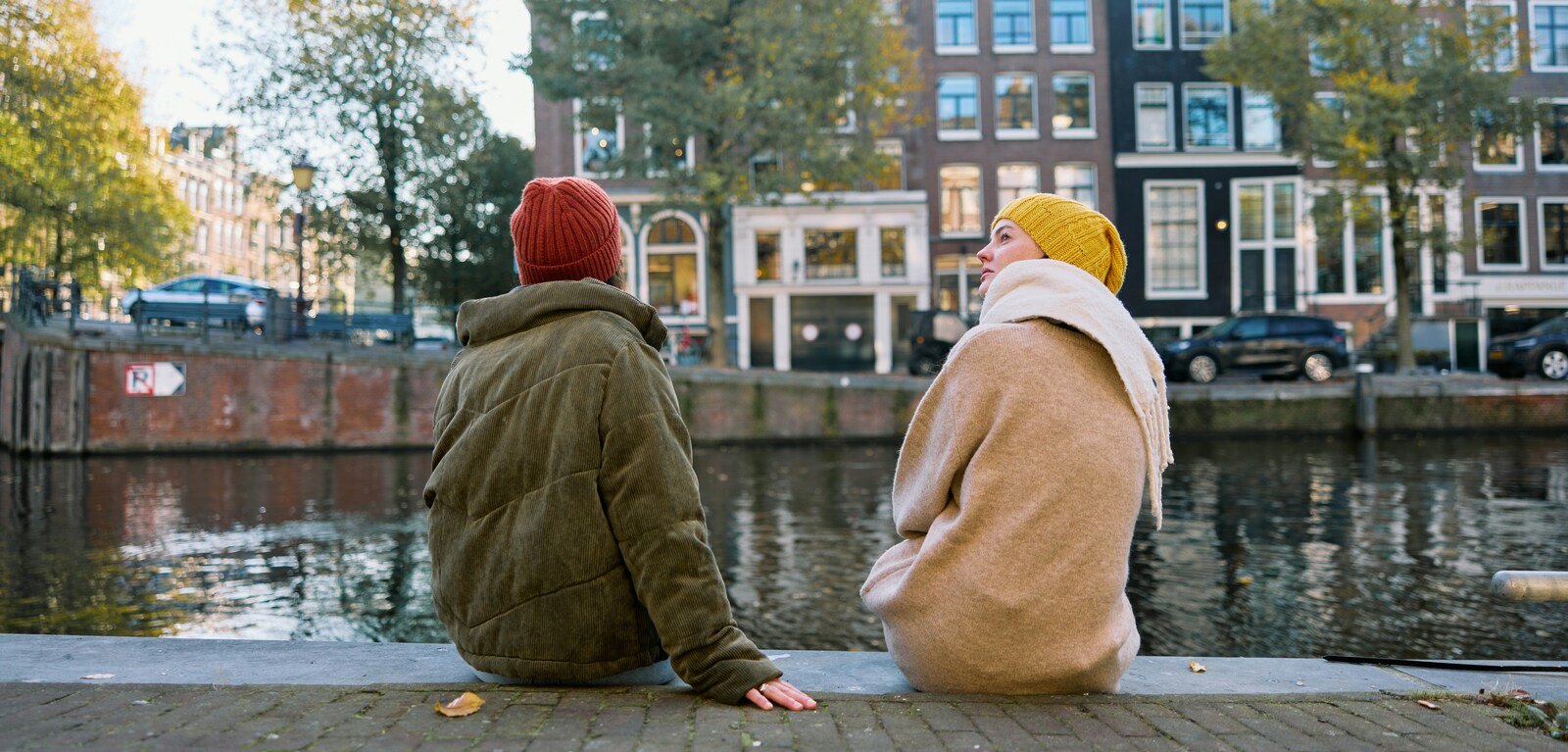 Two people in coats and hats sitting by a river