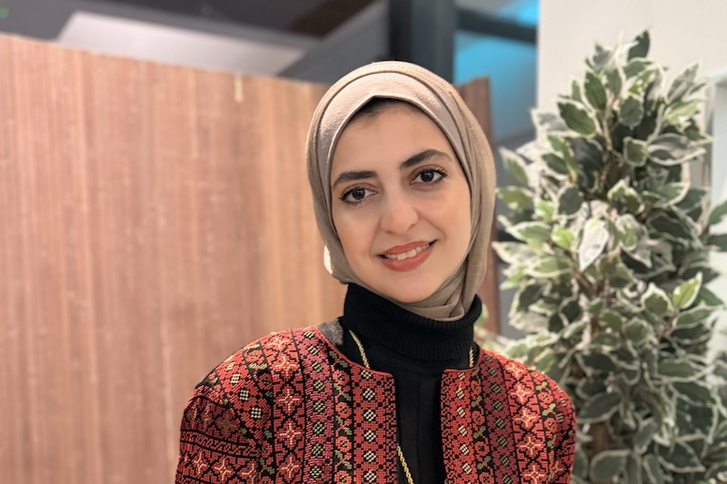 a smiling woman wearing a red patterned jacket and headscarf